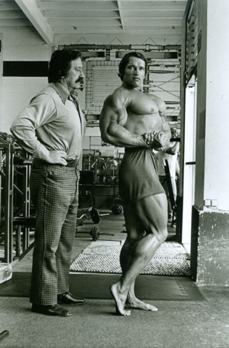 bodybuilder posing in a gym with a trainer observing