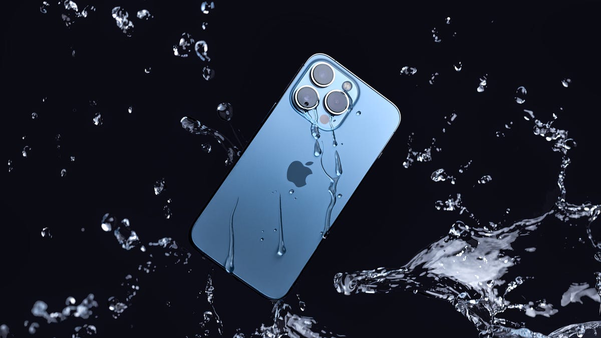 A blue iPhone 13 Pro is splashed with water on a black background