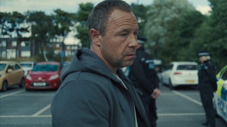 Stephen Graham as Eddie Miller stood in a parking lot near police in Adolescence