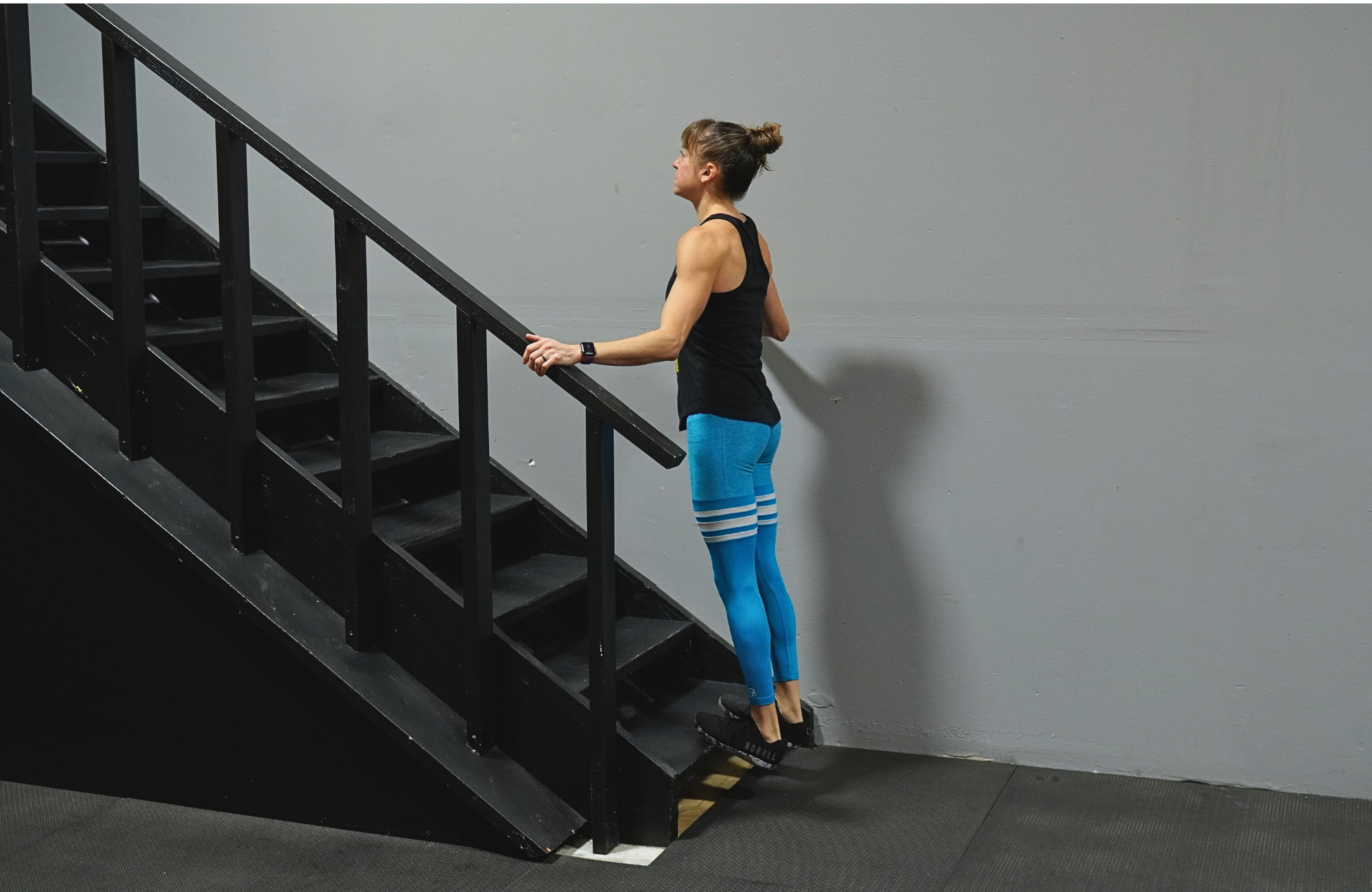 Cori Lefkowith performs a calf raise on a step. She is standing with both feet on the bottom step, heels hanging off the ledge.