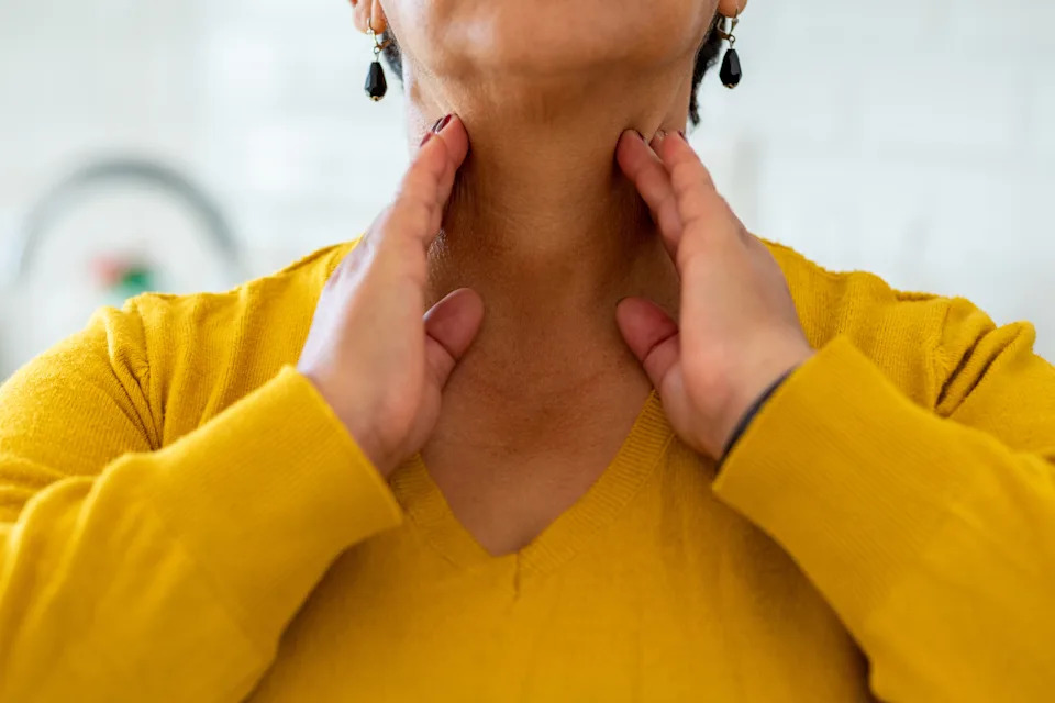 Person gently massaging their neck with both hands, wearing a V-neck sweater and earrings
