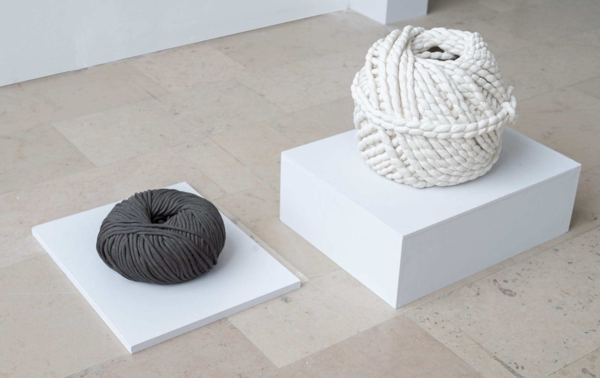 two clay sculptures by Léonore Chastagner of balls of yard, one white and one dark brown