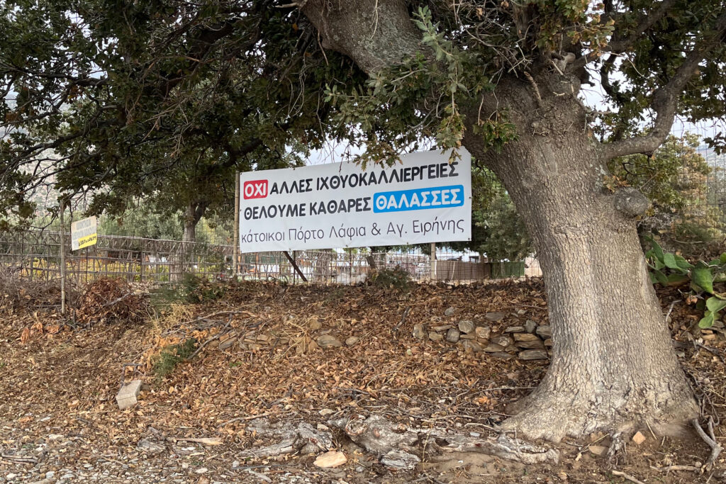 A banner signed by residents from Porto Lafia and nearby Agio Irini reads, “No more fish farms, we want clean seas.” Credit: Moira Lavelle/Inside Climate News