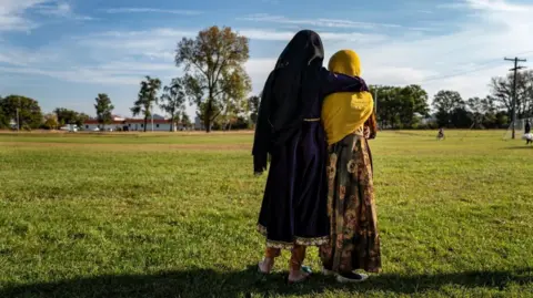 AFP via Getty Images Afghan refugee girls watch a soccer match near where they are staying in the Village at the Ft. McCoy US Army base in 2021 