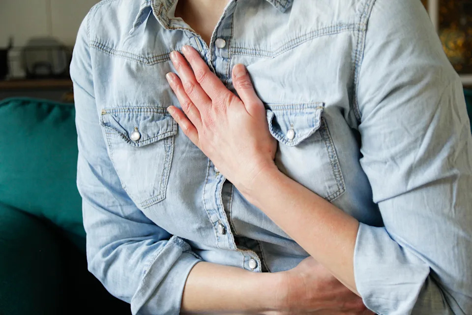 Person in denim shirt holding hand over chest, possibly indicating heartburn or discomfort