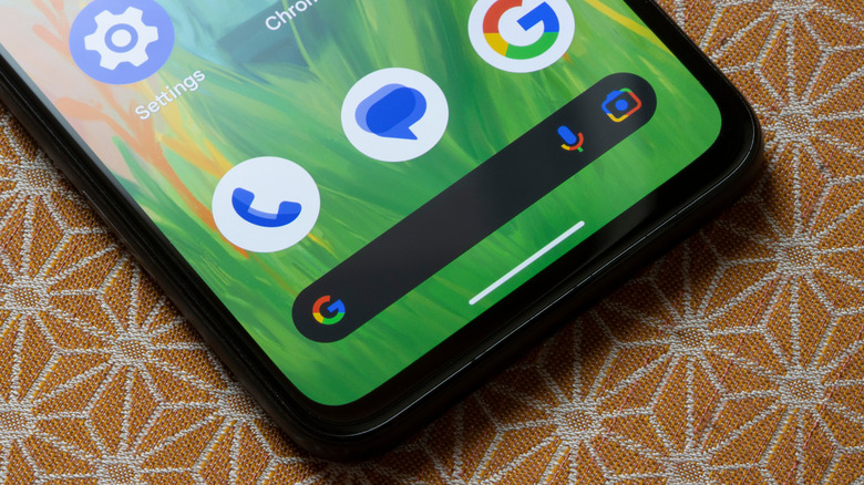 A Google Android phone laying on a patterned table, the phone is displaying the Android Home screen, focusing on a Google widget