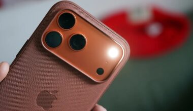 Close-up of a copper-colored smartphone with three rear cameras and a textured protective case held in a hand.