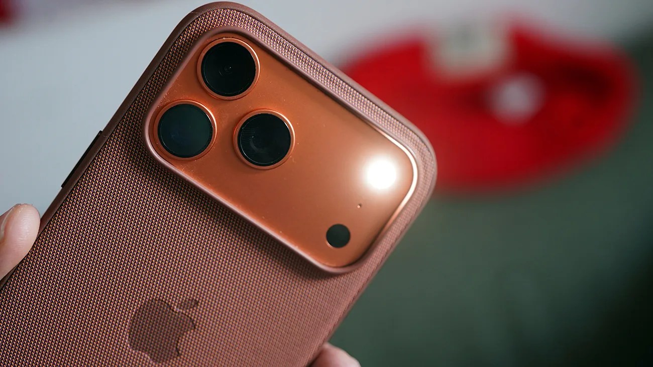 Close-up of a copper-colored smartphone with three rear cameras and a textured protective case held in a hand.