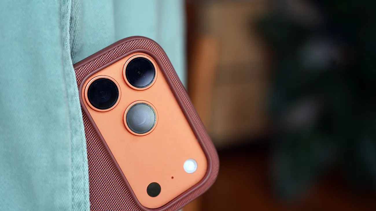 Close-up of a copper-colored smartphone camera module with three lenses and a flash, partially covered by teal fabric.