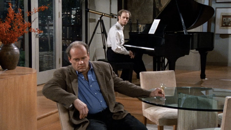 Kelsey Grammer's Frasier Crane sits at his dining table while David Hyde Pierce's Niles Crane sits at the piano in the background in Frasier