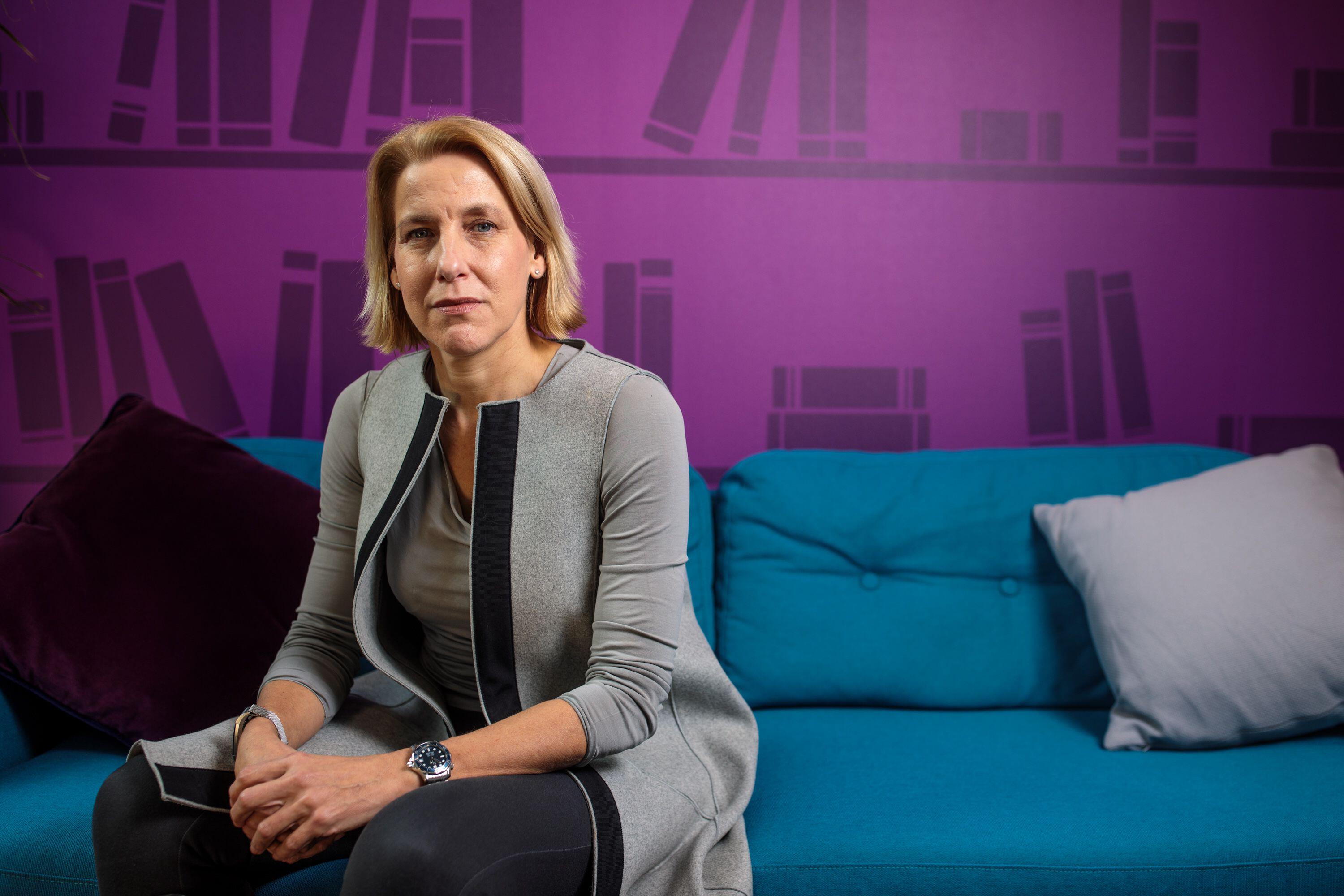 Helen Dickinson, CEO of the British Retail Consortium, sitting on a blue couch in front of a purple wall.