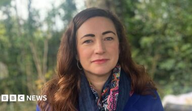 A man wearing a blue-checked shirt with his face buried in his hands