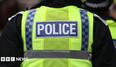 A Police Scotland officer facing away from the camera with the word police on the back of a hi-viz vest.