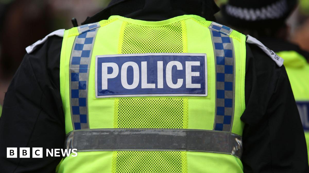 A Police Scotland officer facing away from the camera with the word police on the back of a hi-viz vest.