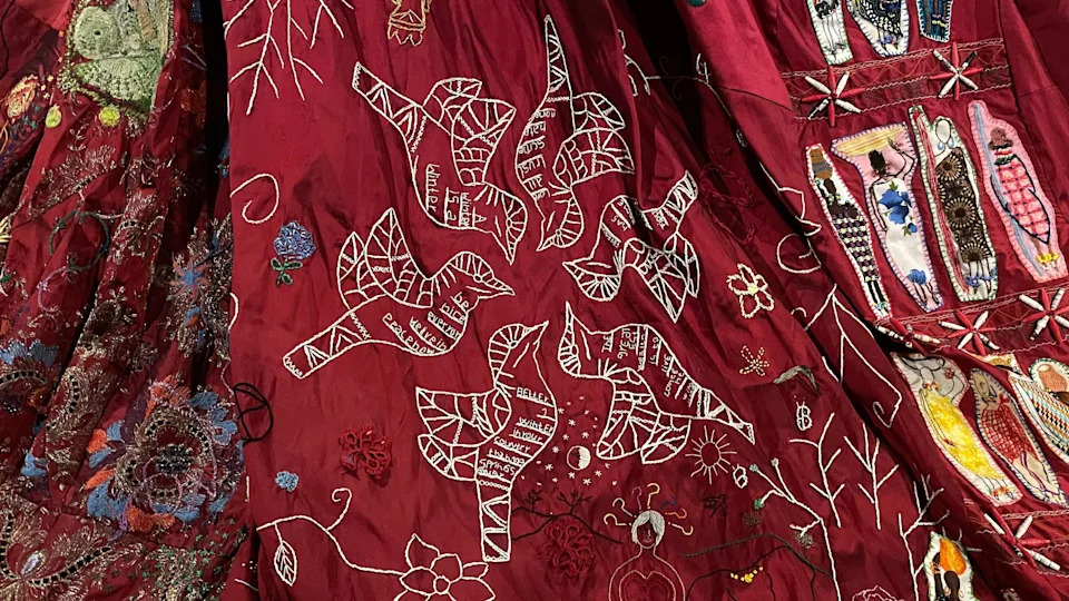 A close up of a panel of the dress showing six doves embroidered in white thread. The doves have phrases in them including “the greatest wealth is to live content with little”, and “A winter in your country is better than a hundred springs away”.