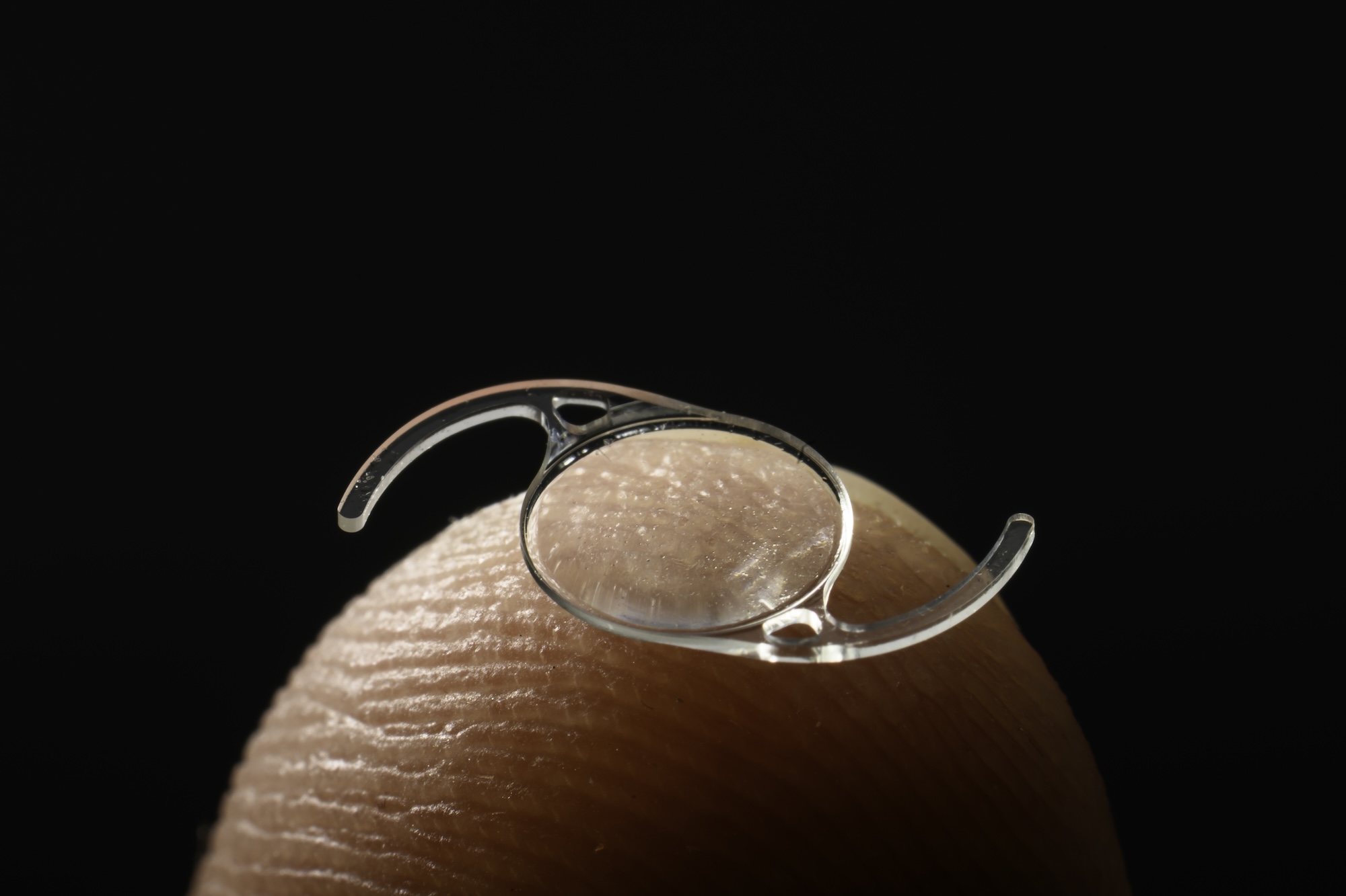 Intraocular lens photographed on a finger tip to show scale.