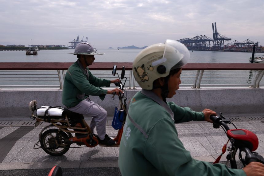 People ride scooters past the Yantian port in Shenzhen, Guangdong province, China, on October 30, 2025.