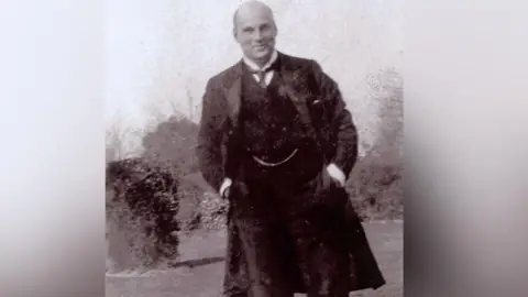 West Sussex Record Office A black and white photo of a man in a long black coat.