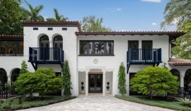 a white, Mediterranean-inspired mansion sits behind naturally manicured trees
