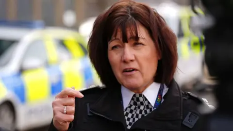 PA Media Jo Farrell, a woman with reddish-brown hair in a Police Scotland uniform, is standing talking to someone outside. A police car is in the background.