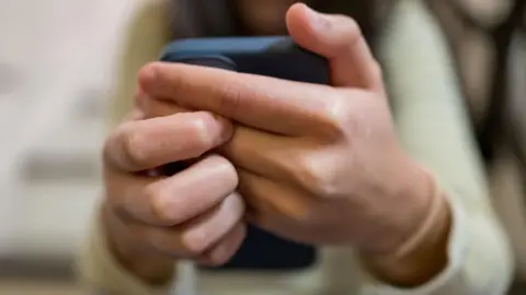 Getty Images A close-up of a woman's hands clasping a smartphone in front of her.