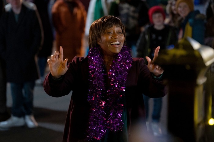 Yolande conducts a choir with some pink tinsel around his neck in EastEnders
