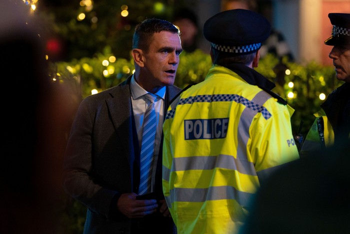 Jack Branning - wearing a suit- talks to a police officer in Albert Square in EastEnders