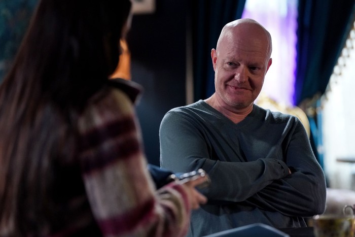 Max, wearing a blue jumper, smiles towards Lauren in EastEnders