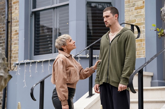 Nicola, wearing a beige blouse, holds her hand out to a shell-shocked Harry who stands on the steps outside of No. 1 Albert Square in a green hoody in EastEnders