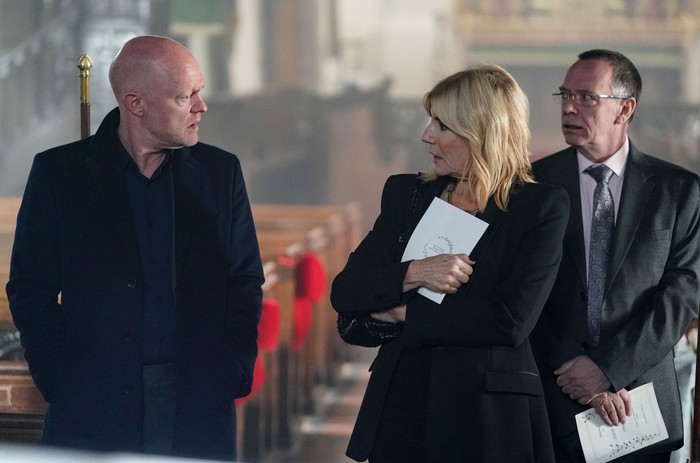 Ian looks on as Cindy confronts Max in the church in EastEnders. The trio are all wearing dark suits.