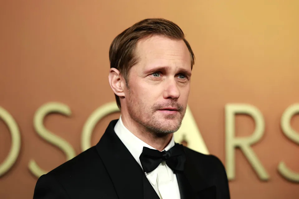 Man in formal tuxedo at an event with "Oscars" partially visible in the background