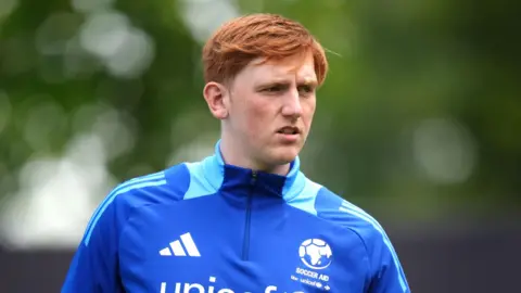 PA Media Angry Ginge wear a blue soccer aid half zip top which has lighter blue markings on the neck