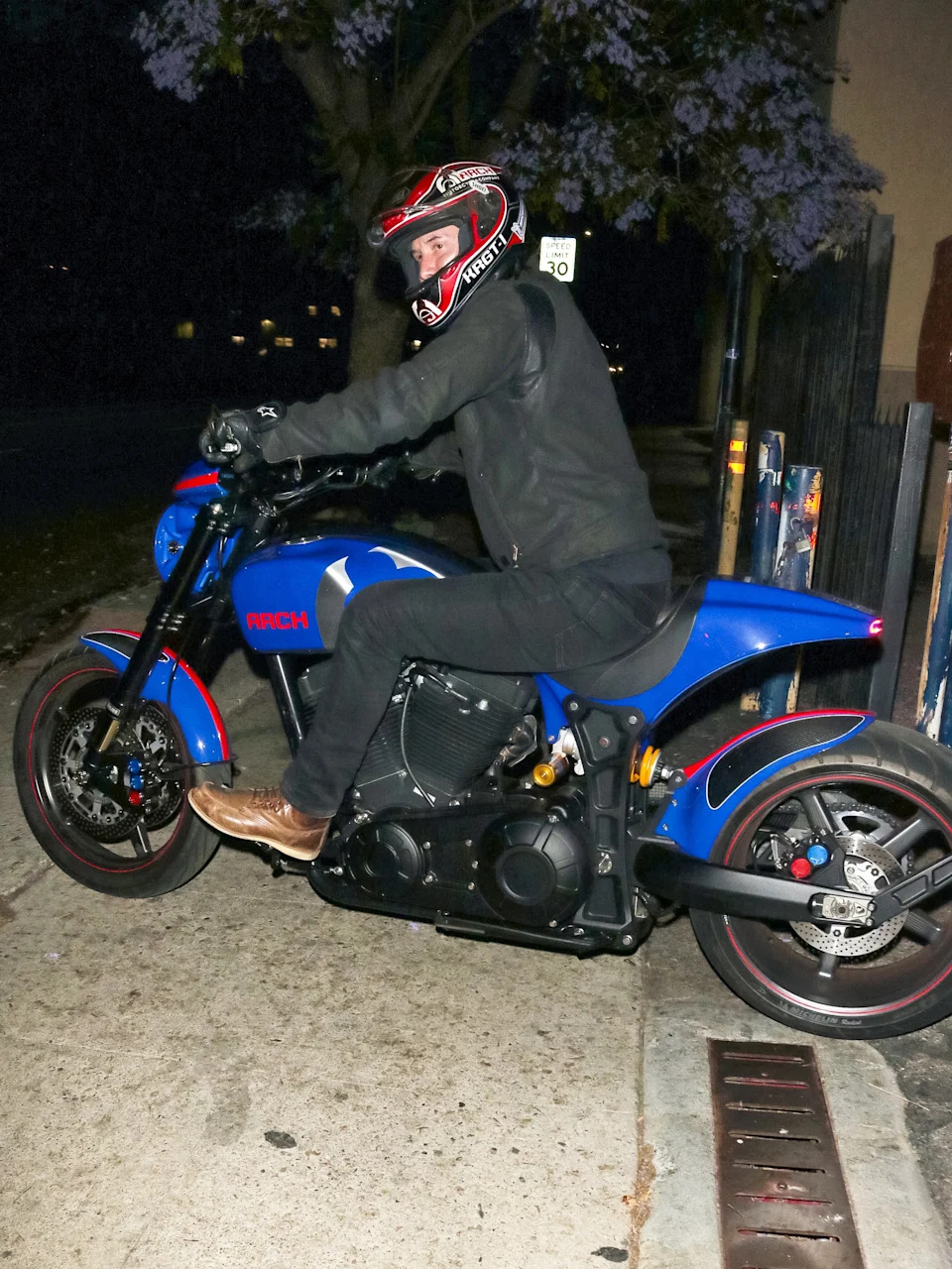 Person in motorcycle gear sitting on a blue motorcycle on a street at night