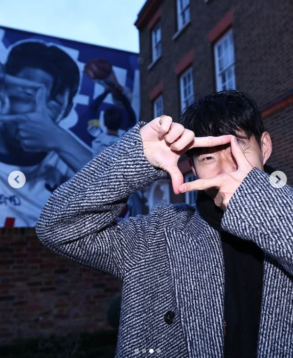 Former Tottenham Hotspur player Son Heung-min poses with his signature camera clicking hand gesture in front of a mural outside of the Totthenham Hotspur Stadium in London in this screen capture from Tottenham Hotspur's Instagram. [SCREEN CAPTURE]