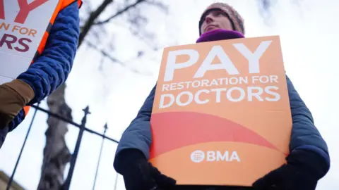 PA Media Doctors dressed in outdoor winter clothes hold strike posters - one says, "Pay restoration for doctors"