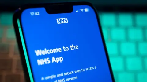 Getty Images A phone with a blue screen on it. The screen has white writing on reading "Welcome to the NHS app".