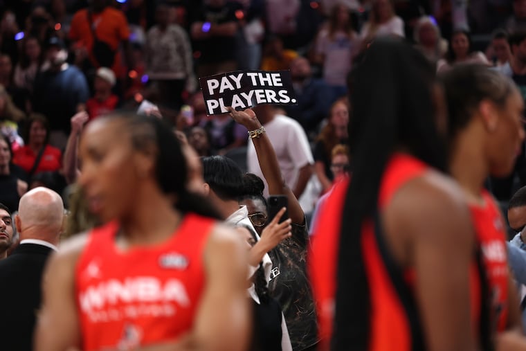 A fan holds a sign saying "Pay the players" during the 2025 WNBA All-Star Game. Especially in this era of legalized sports betting, there's never been more scrutiny on WNBA players, who argue that their compensation isn't commensurate with that of their male counterparts.