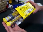 FILE - In this July 8, 2016, file photo, a pharmacist holds a package of EpiPens epinephrine auto-injector, a Mylan product, in Sacramento, Calif. Insurers will sometimes choose to cover a significantly more expensive drug or device, such as AUVI-Q, even when there’s a cheaper alternative on the shelf. (AP Photo/Rich Pedroncelli)