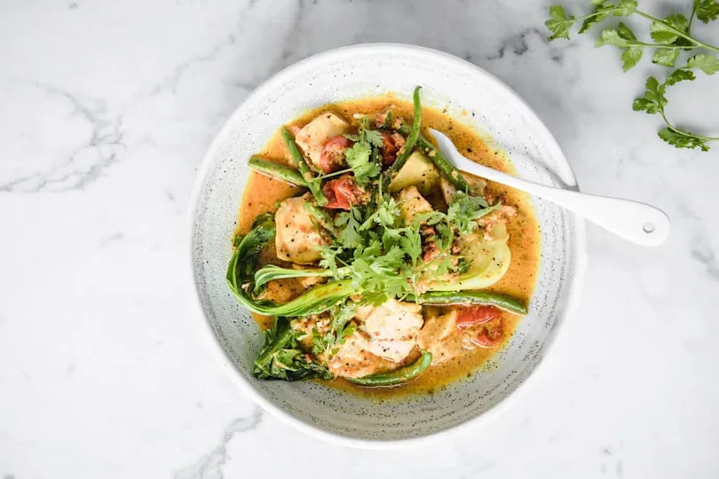 Curry salmon with coconut milk and bok choy in a bowl with a fork.