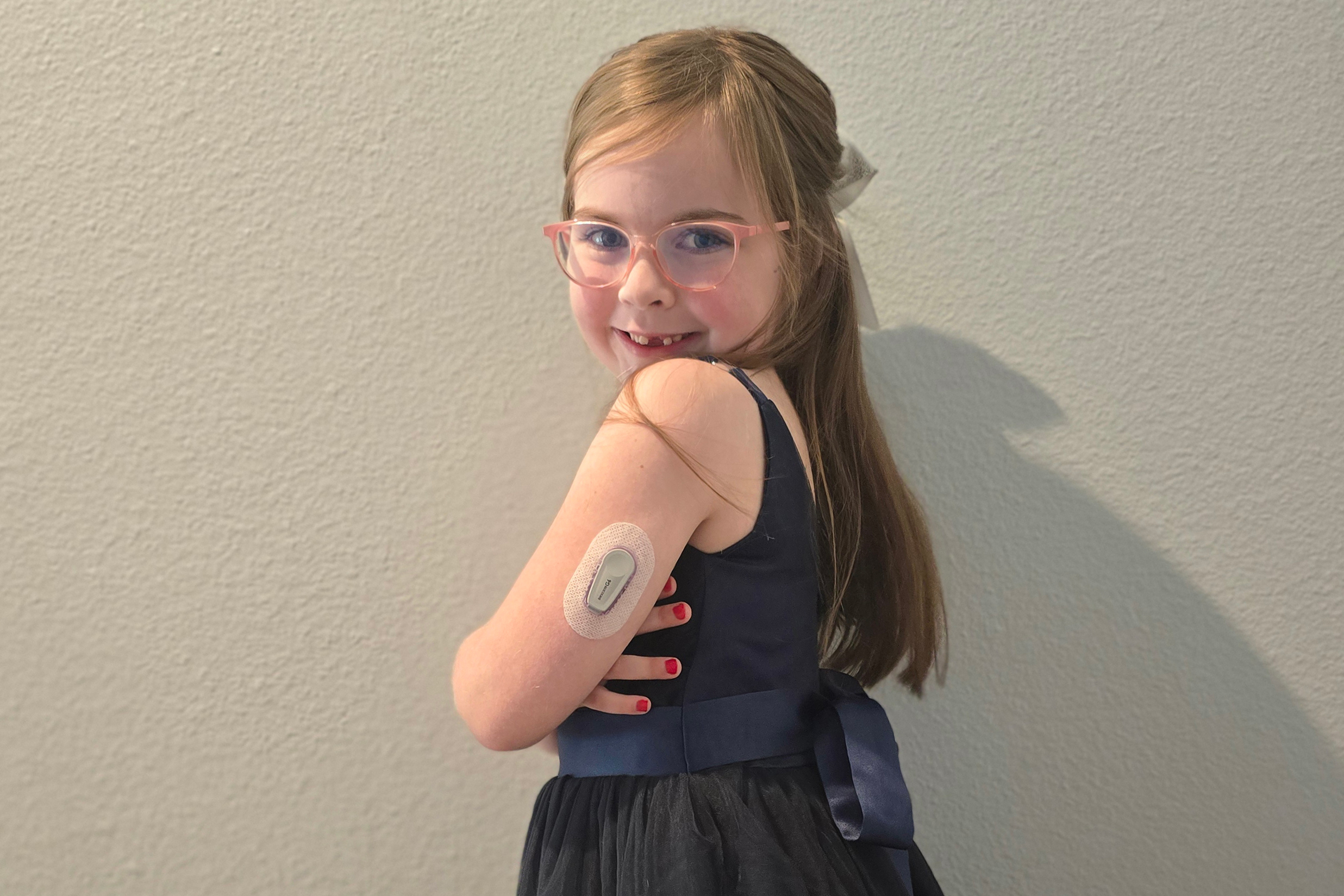 A 6-year-old girl poses for a portrait showing her glucose monitor on her arm.