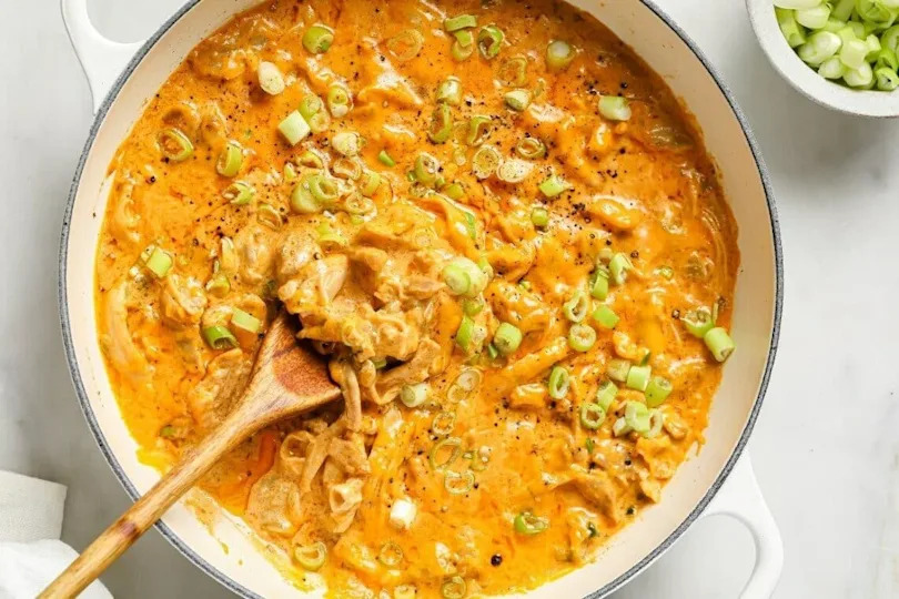 Green chile chicken in a pan with a wooden spoon.