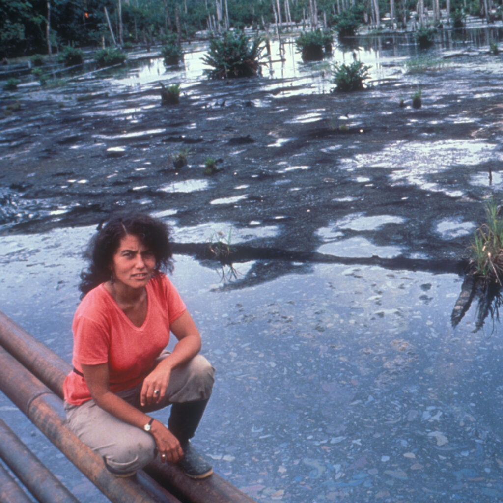 Judith Kimerling kneels on pipelines above a drilling waste pit in the Ecuadorian Amazon in July 1990. Credit: Courtesy of Judith Kimerling
