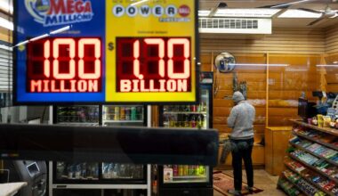 A convenience store employee prays while Jackpot payouts for Powerball and Mega Millions are displayed outside the store, Tuesday, Dec. 23, 2025, in New York. (AP Photo/Yuki Iwamura)