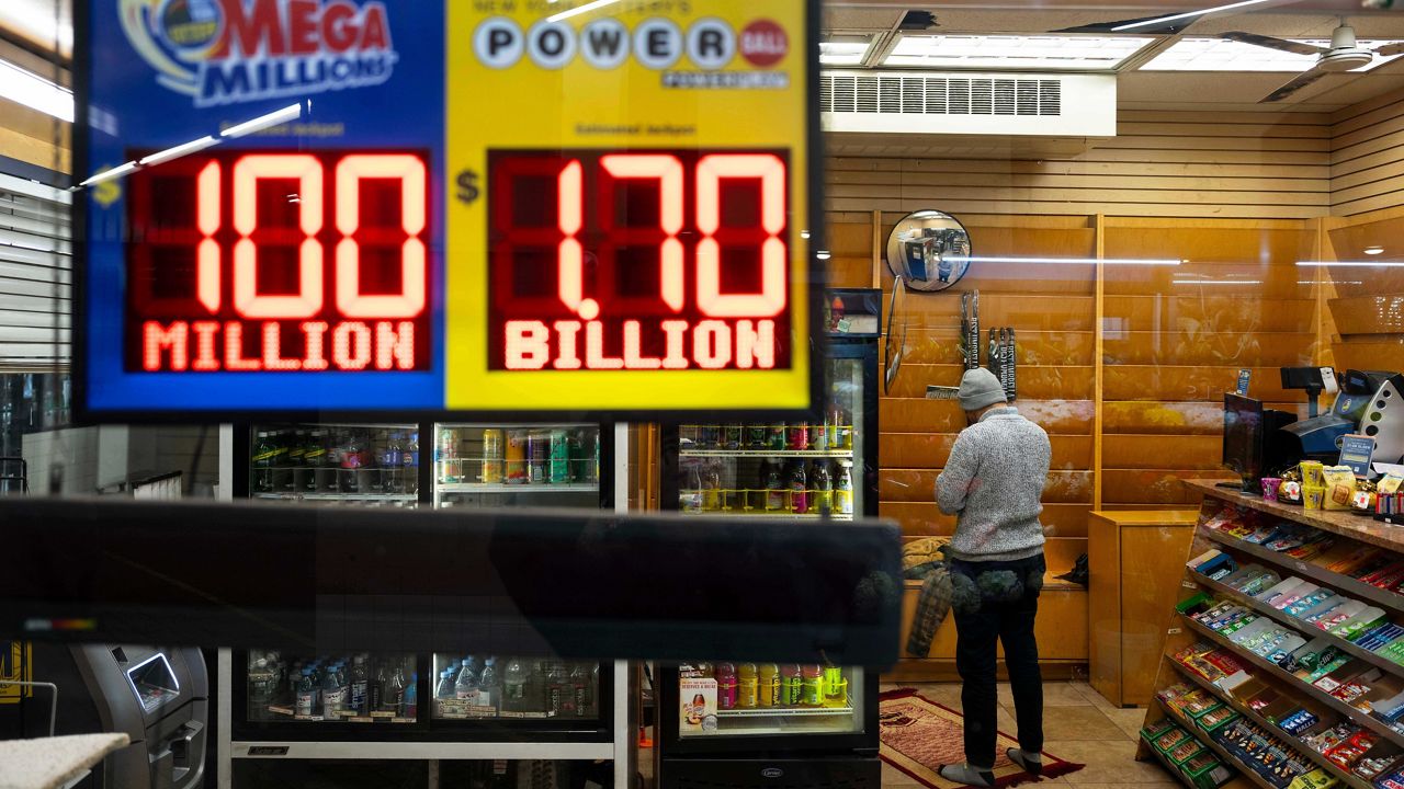 A convenience store employee prays while Jackpot payouts for Powerball and Mega Millions are displayed outside the store, Tuesday, Dec. 23, 2025, in New York. (AP Photo/Yuki Iwamura)