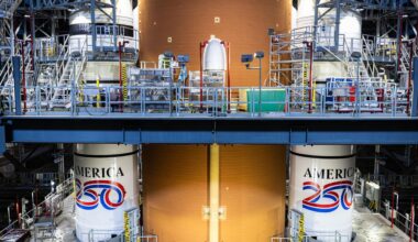 An image from inside a warehouse shows two tall white cylinders on either side of a yellow taller cylinder. The two white cylinders have red, white and blue paint with the words 'America 250' on them.