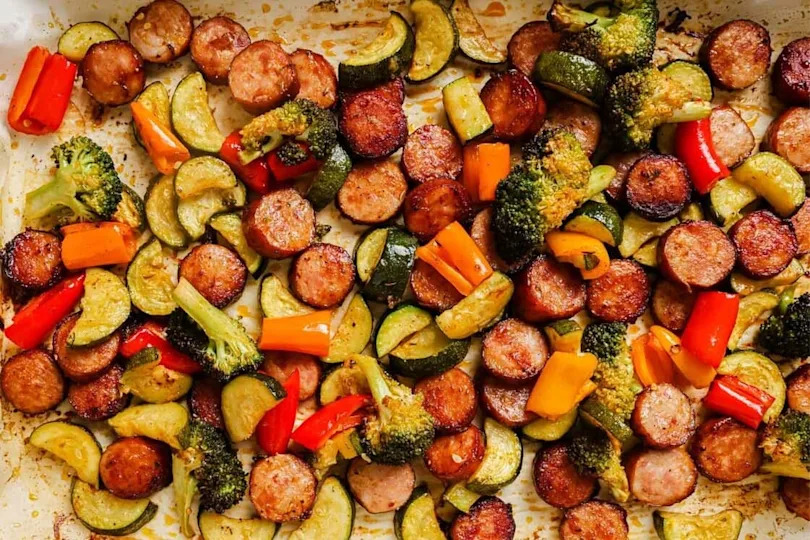 Sausage and veggies sheet pan dinner with a spoon.