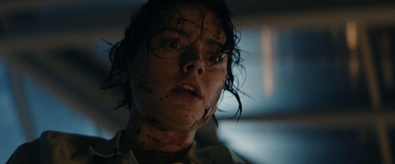A person with wet hair and a blood-splattered face looks up with a shocked expression in a dimly lit setting.