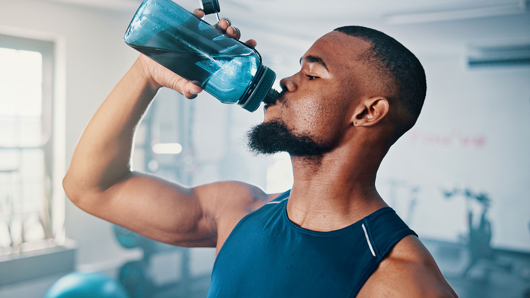 A close-up picture of a young man drinking water from a bottle in the gym