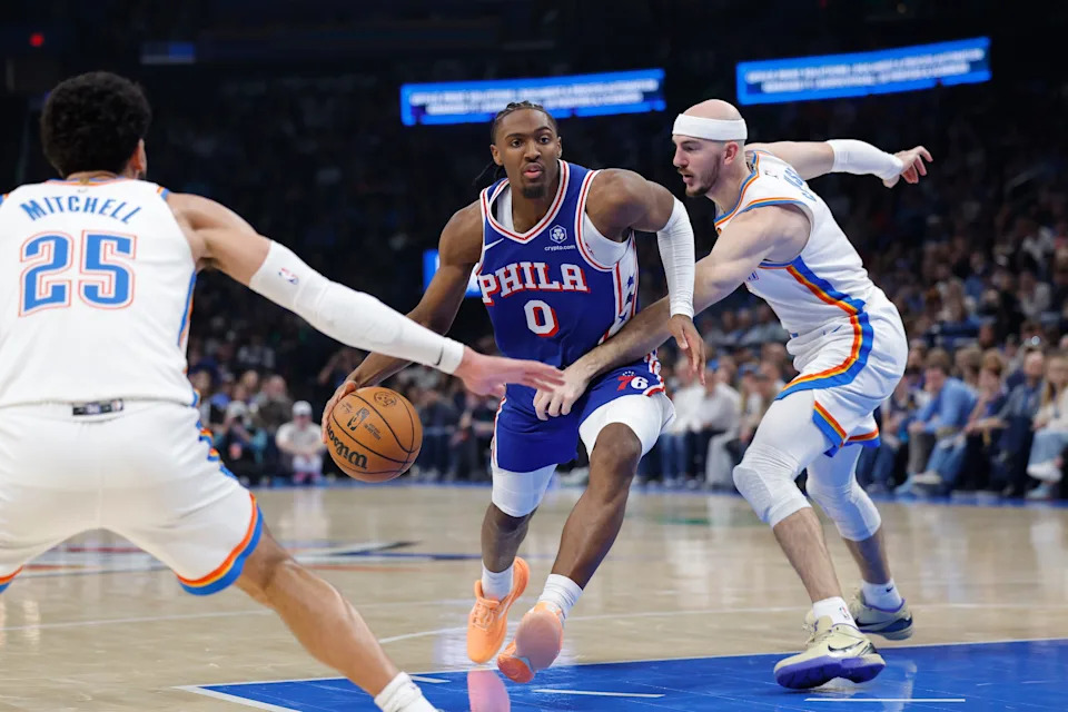 Dec 28, 2025; Oklahoma City, Oklahoma, USA; Philadelphia 76ers guard Tyrese Maxey (0) drives between Oklahoma City Thunder guard Ajay Mitchell (25) and guard Alex Caruso (9) during the second quarter at Paycom Center. Mandatory Credit: Alonzo Adams-Imagn Images
