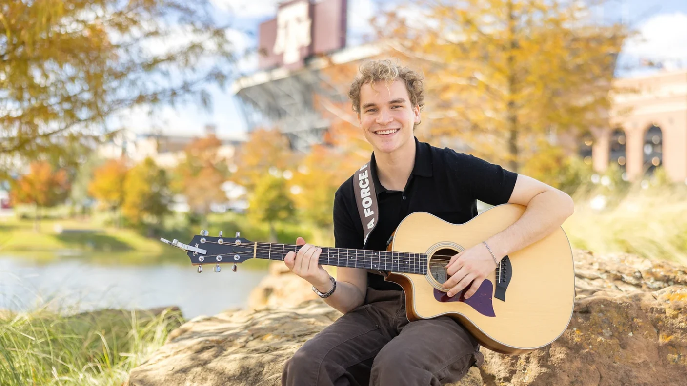 Portrait of Aiden Ross holding his acoustic guitar in Aggie Park